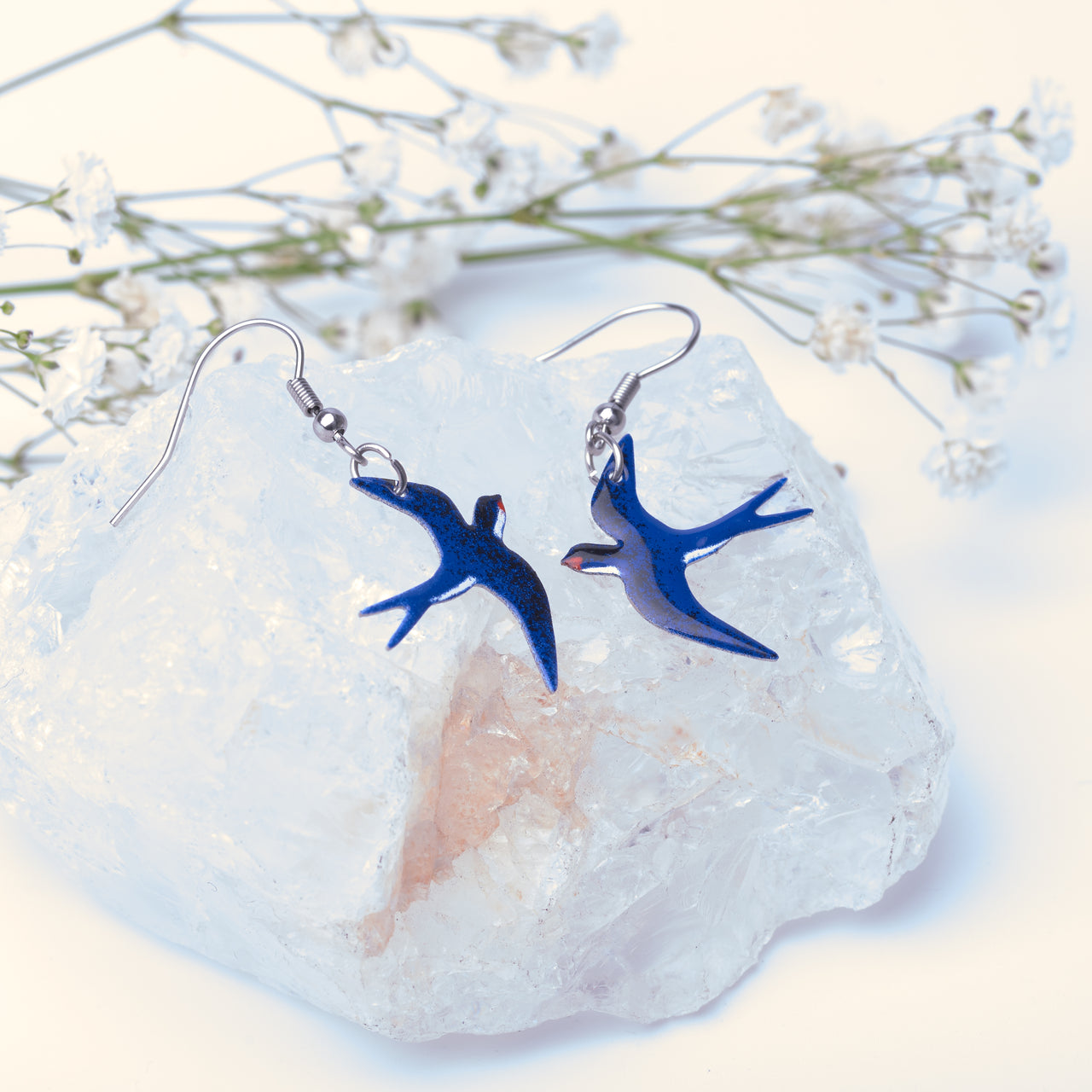 a pair of blue handmade swallow earrings are resting on a crystal