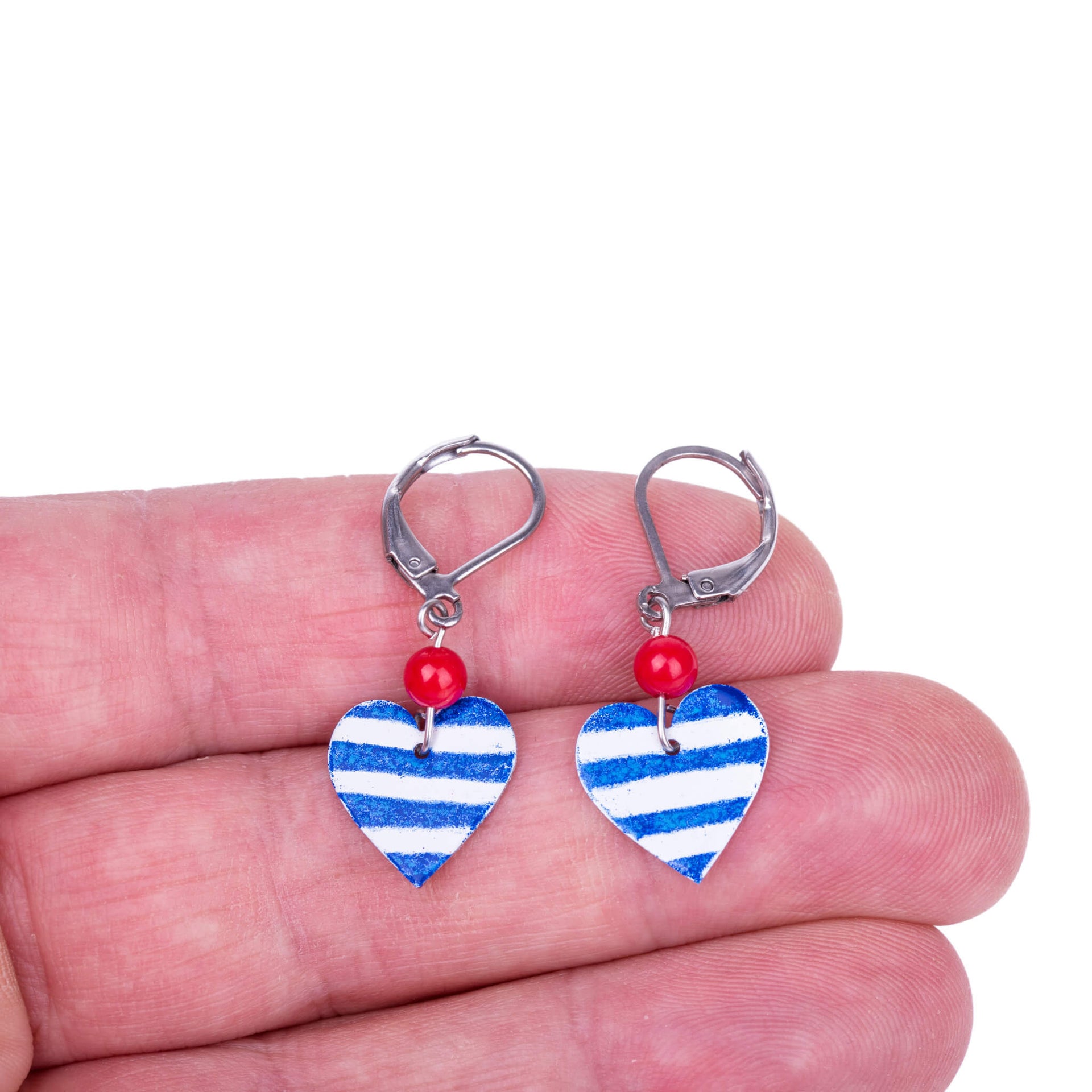 handmade heart earrings with blue stripes and red coral beads show on fingers
